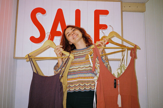 Woman smiles holding dressed in front of Sale sign 