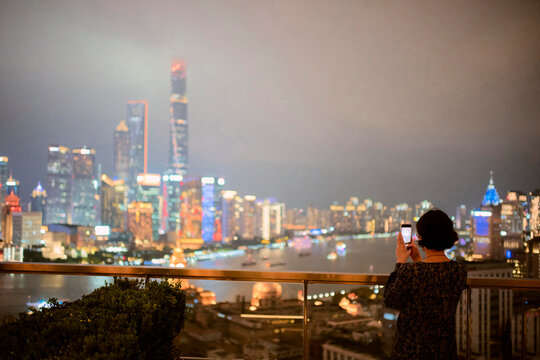 View of Shanghai Skyline at Night With a Woman Taking a Photo