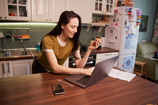 Woman working on laptop in kitchen while holding snack