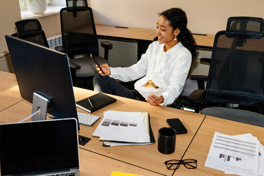 Businesswoman Using Smartphone While Eating Lunch at Office Desk