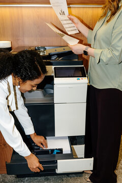 Office workers loading paper into printer while reviewing documents