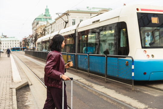 Traveler with suitcase walking past a modern tram in European city