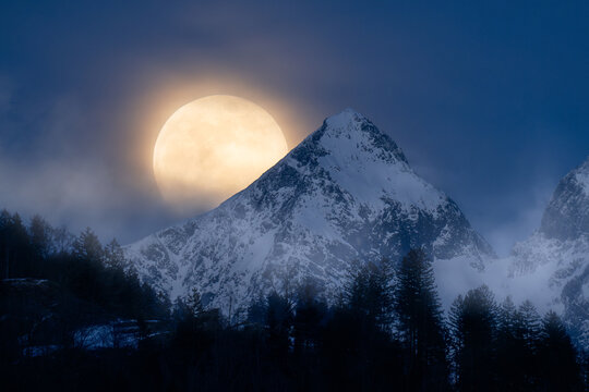 Full moon setting behind misty alpine peak, Swiss Alps