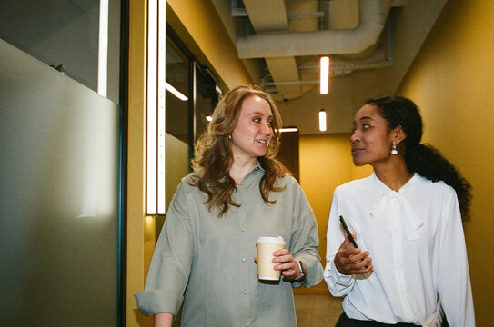 Two Businesswomen Walking and Talking in Modern Office Hallway