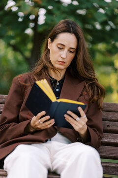 Woman Reads Book While Sitting on a Park Bench in the Afternoon Sun