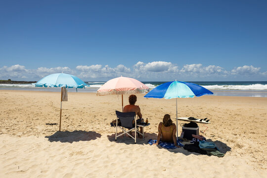 Friends under beach umbrellas in summer in Yamba Australia