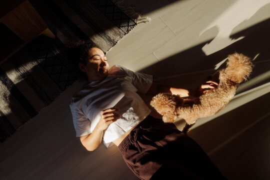 A young woman lies on the floor and pets her dog