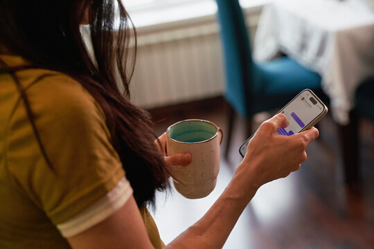 Woman holding a cup and using a phone indoors