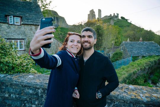Couple taking a selfie in front of the ruins of Corfe Castle, England
