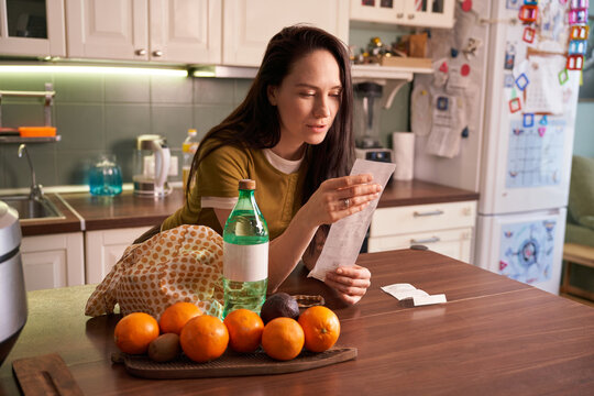 Woman checking receipt in kitchen while surrounded by fruits