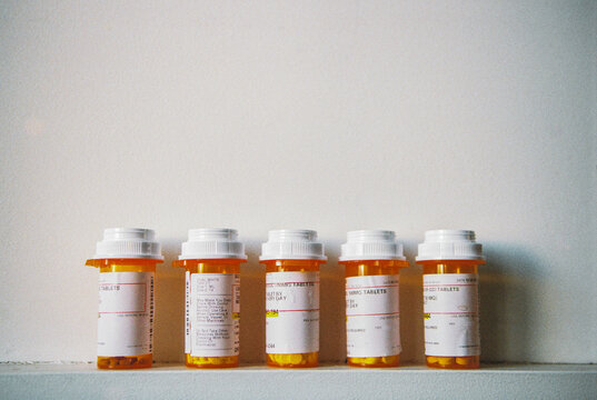Row of five prescription pill bottles on a bathroom shelf