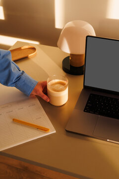 Hand reaching for coffee beside laptop on desk
