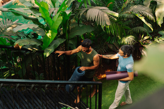 Two People Carry Yoga Mats in a Garden Setting During Daylight