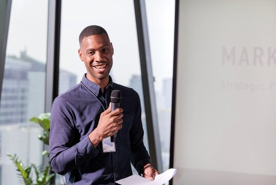 Smiling speaker presents marketing strategy with microphone and notes.