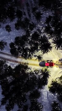 Top-down aerial view of a snowcat machine driving on a trail in a snowy forest at night