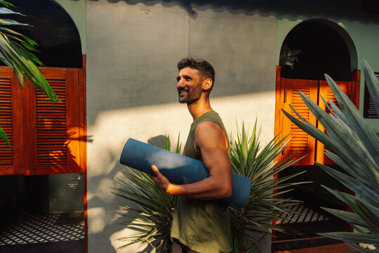 Man Carries Yoga Mat in Sunny Tropical Setting Outdoors