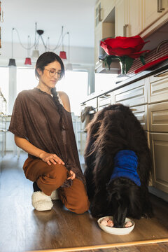 Woman kneeling in a kitchen while her Afghan Hound is eating