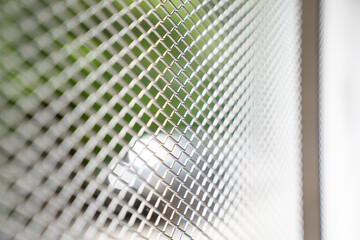 Obraz premium Metal mesh screen with diamond shaped openings. Silver grid pattern looks clean, modern, and strong, with soft green outdoor blur behind it.