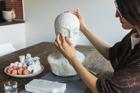 Female artist sculpting a human head bust with clay