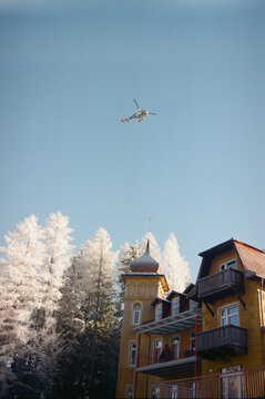 Helicopter flying above buildings and snowy trees under a clear sky