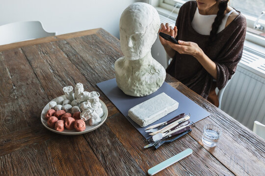 Artist using a smartphone while working on a clay sculpture
