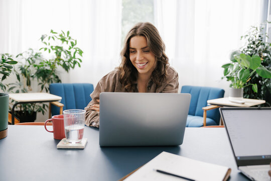 Woman Works on Laptop While Sitting at Table in Bright Office