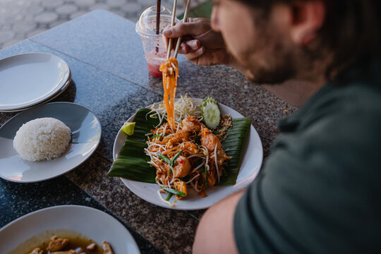 Person eats pad thai at a restaurant in an outdoor setting