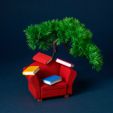 miniature books above a red armchair, a tree rising behind