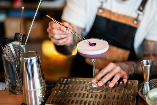 Bartender garnishing cocktail with purple foam and floral elements