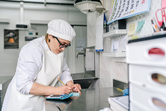 Female artisan cheesemaker calculating expenses in dairy factory