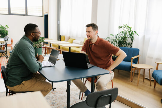 Two Men Have a Discussion at a Table in a Workspace