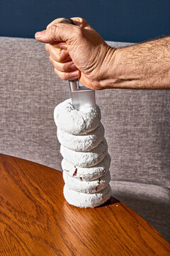 Hand Stabbing Tall Stack of Powdered Sugar Donuts with Knife