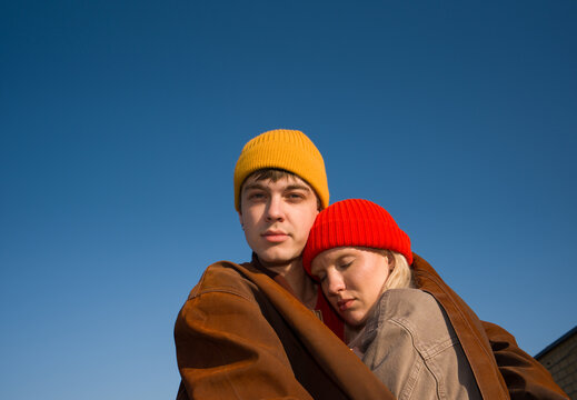 Young Couple Hugging in Hats Against Clear Blue Sky