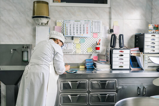 Artisan cheesemaker calculating costs in small dairy factory interior