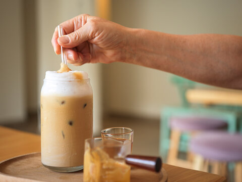 Hand Stirs Ice Coffee Drink in Glass Cup on Wooden Table