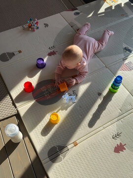 Baby plays on mat with colorful toys in sunlight