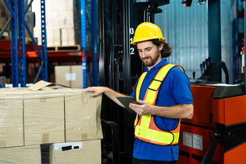 warehouse man in helmet vest using digital tablet to verify cargo quantity with hand placed on pallet of packed boxes near forklift in industrial storage area during routine inspection © Ekkasit A Siam