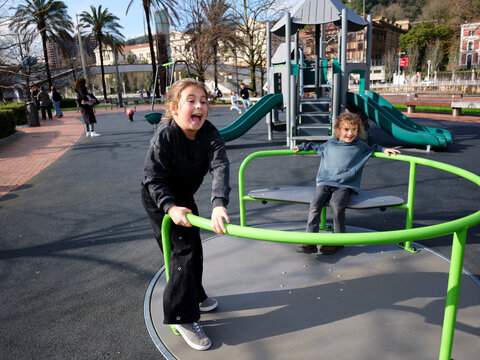 Cheerful young child pushing merry go round with another child smiling