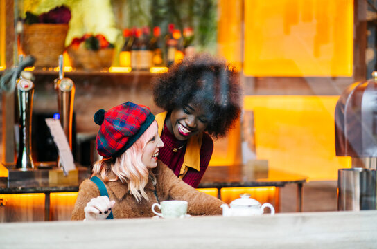 Diverse young women laughing and drinking tea at cafe