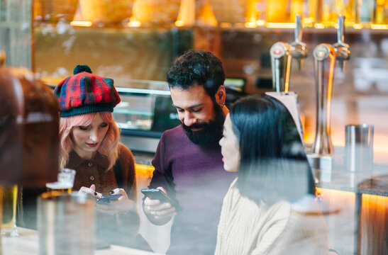 Diverse friends connecting and using smartphones at bar