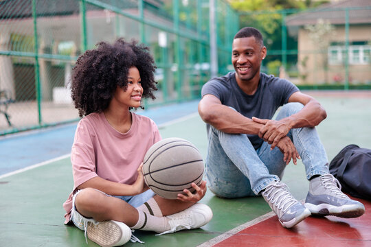 Smiling pair relax on basketball court with ball.