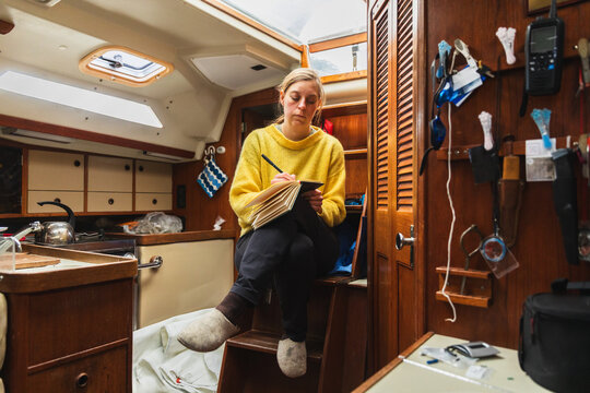 Female sailor writing her personal travel diary in a sailboat cabin