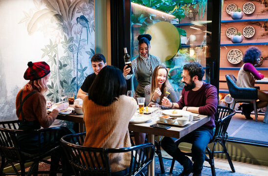 Friends enjoying dinner and drinks with a waitress serving wine