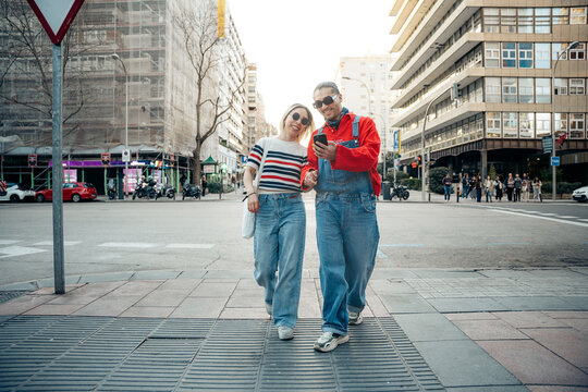 Happy couple walking city street using smartphone