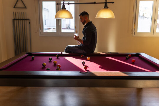 Man sitting on billiard table drinking with dramatic light