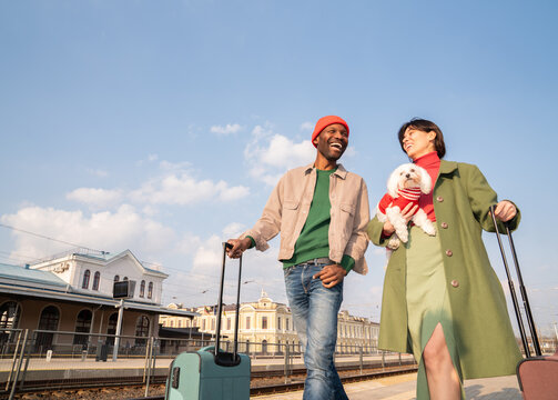 Couple Walks With Luggage and Dog at Train Station on Sunny Day