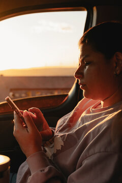 Woman using smartphone inside vehicle during golden hour