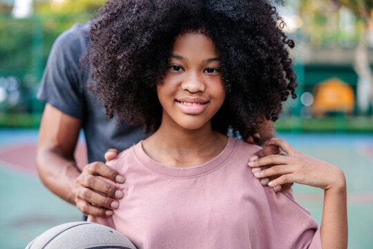 Father and daughter with basketball, smiling on the court.