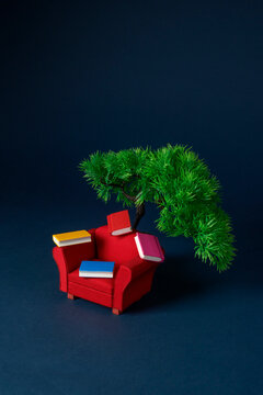 a red armchair with books below a small tree on blue