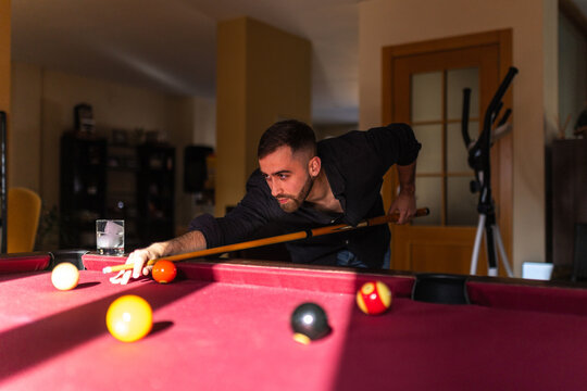 Elegant man playing billiards aiming shot at home